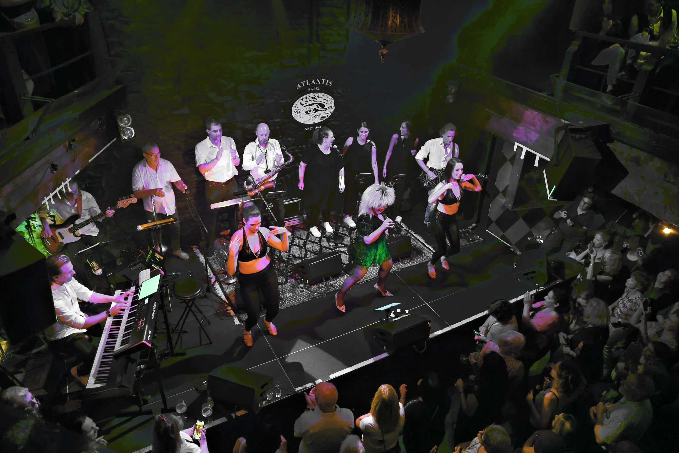 Blick von oben auf Sängerin, zwei Tänzerinnen und Band auf der Bühne.
